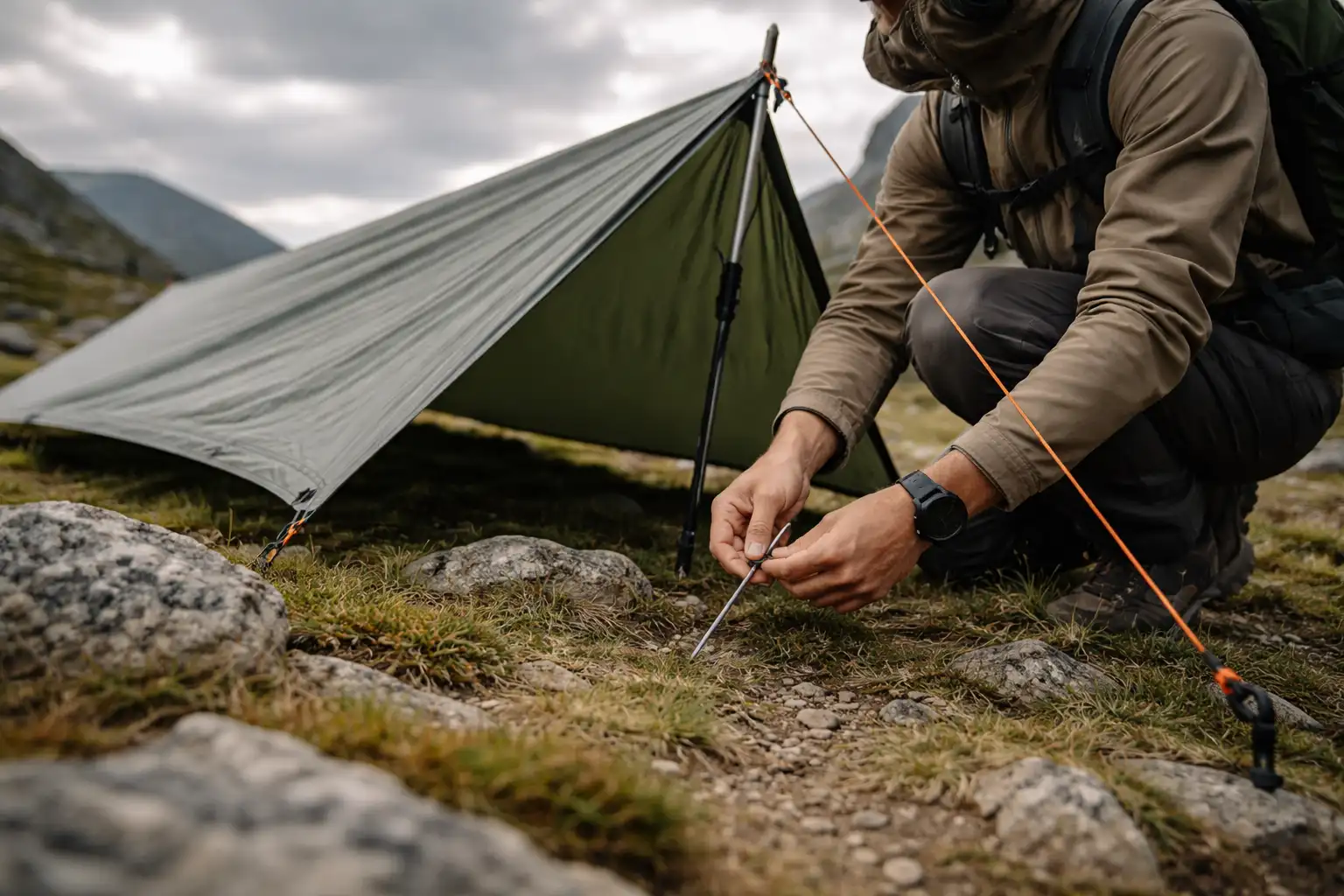 Randonneur vérifiant les sardines et les haubans d'un tarp sous un ciel nuageux